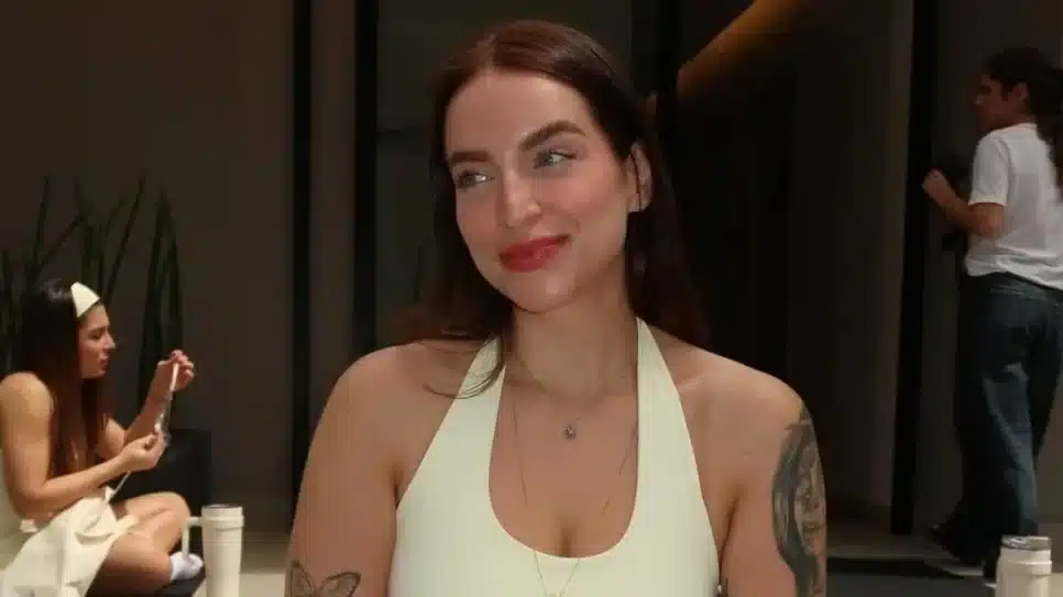 mulher, branca, de olhos azuis, cabelos lisos e castanhos, usando uma roupa de academia amarela, sorrindo