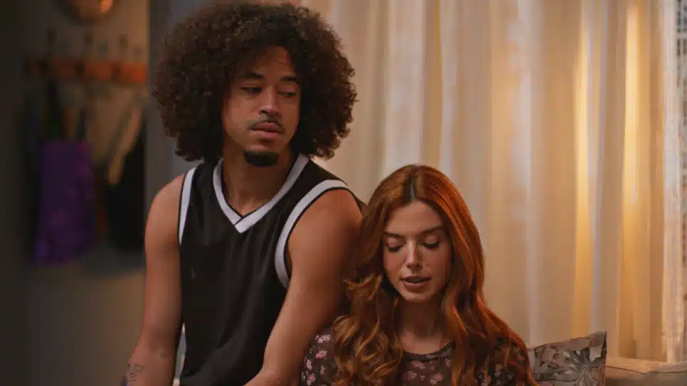 Ryan sentado no braço do sofá com Kami sentada no sofá, ambos com rosto mais sério em cena de "Dona de Mim"