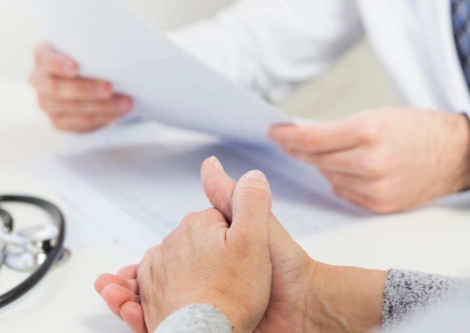 Médico segurando exame enquanrto paciente espera com maõs entrelaçadas