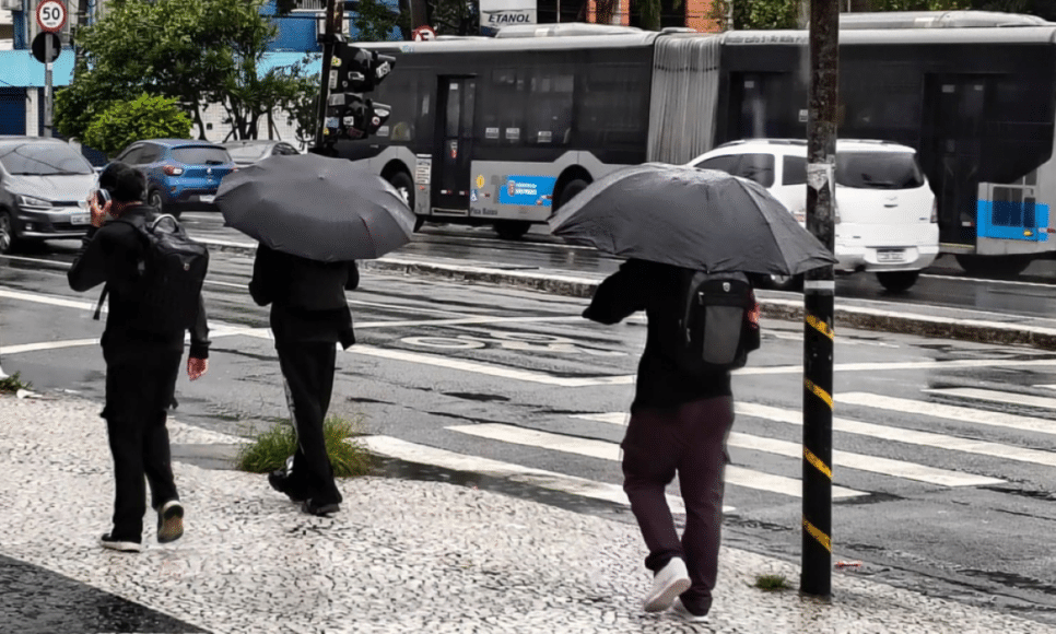 Pedestres se protegem da chuva nas ruas do Jardim Consórcio, na zona sul da cidade de São Paulo, na manhã desta quinta-feira (12)